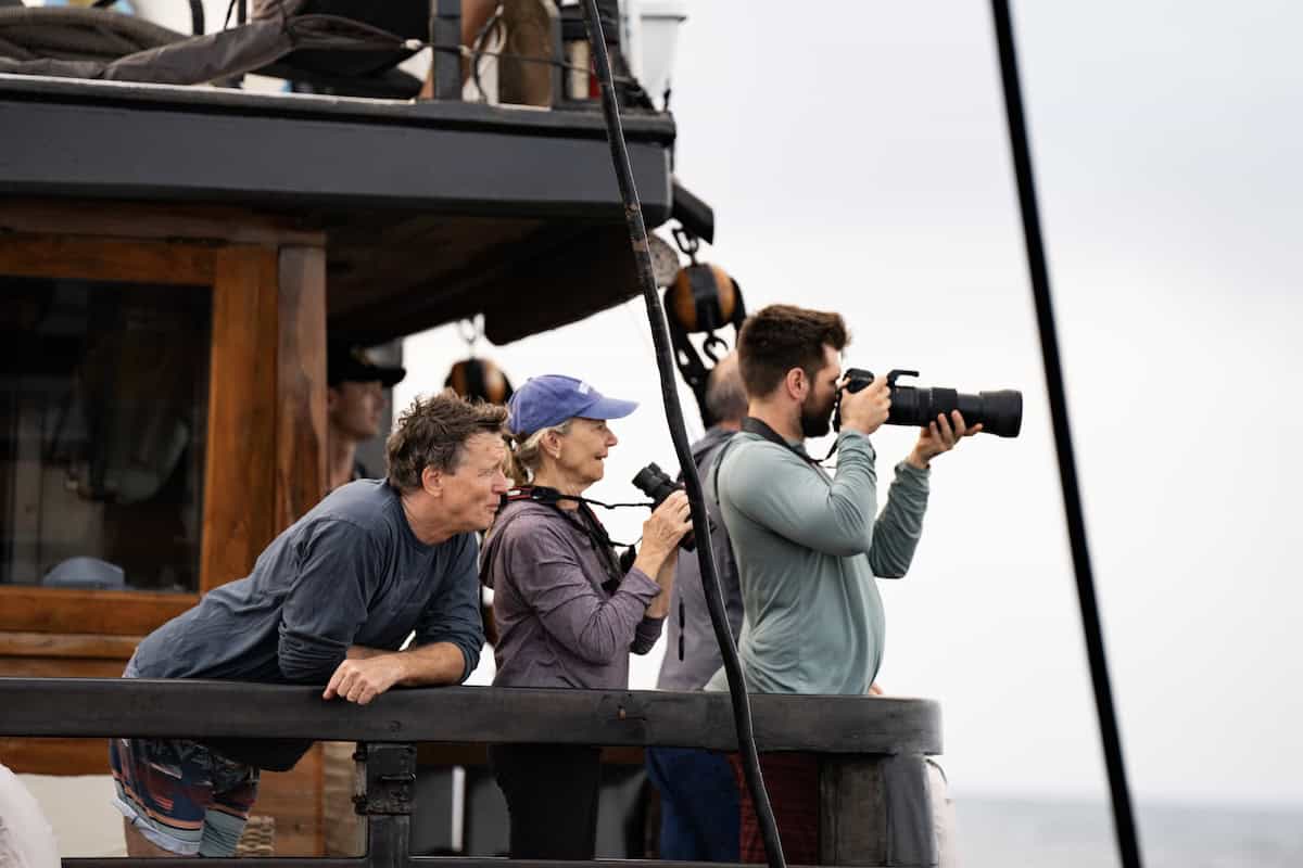 Travelers standing on bow of ship with binoculars and telephoto lenses while on whale patrol in Banda Sea