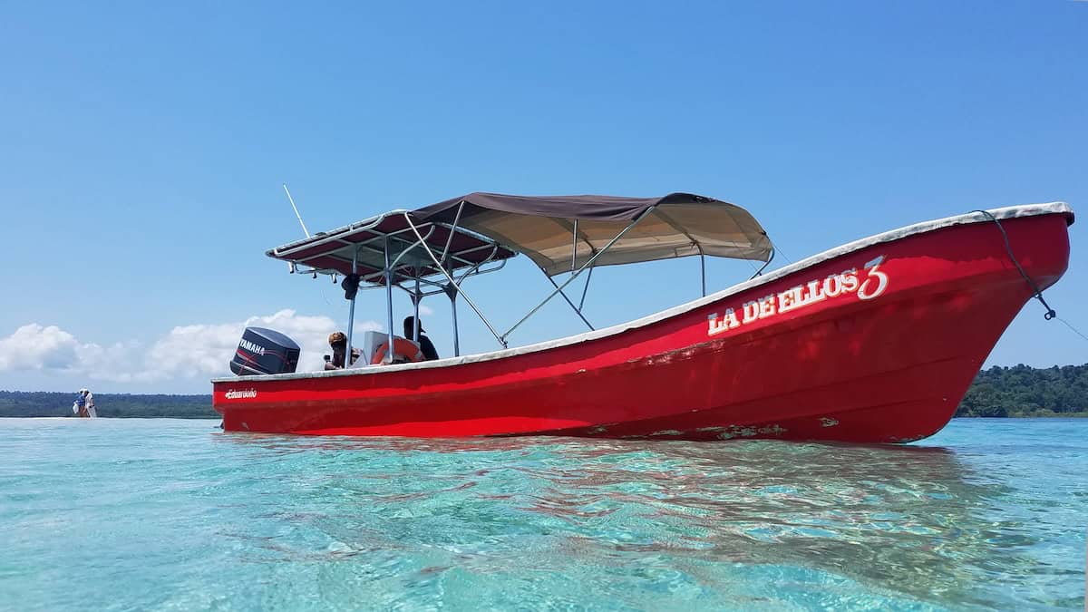 Snorkeling boat anchored in shallow, crystal-clear waters off the coast of Panama, surrounded by tropical coral reefs and calm ocean.