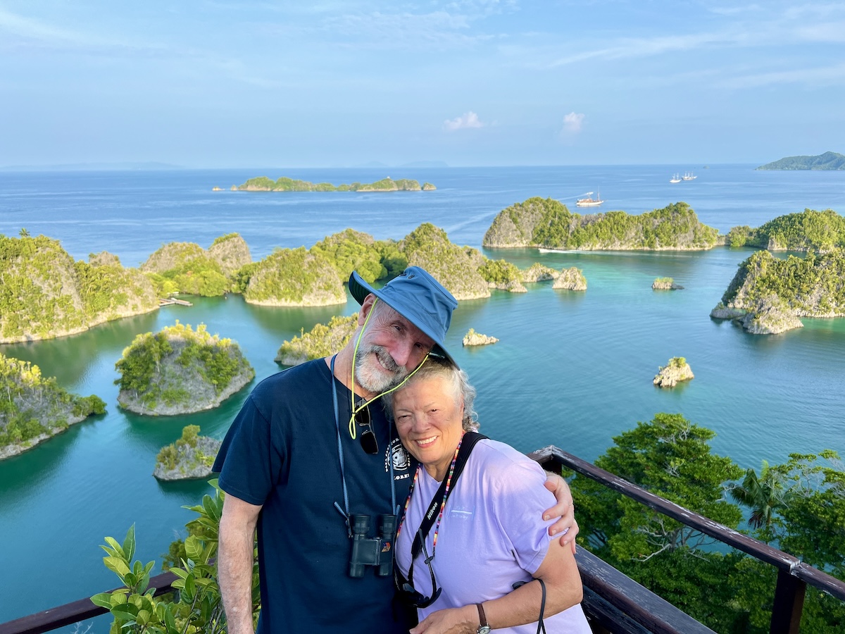 A couple taking in the iconic limestone islands of Piaynemo Viewpoint in Raja Ampat’s Fam Islands, where turquoise waters and forest-covered karst islands stretch across the horizon.