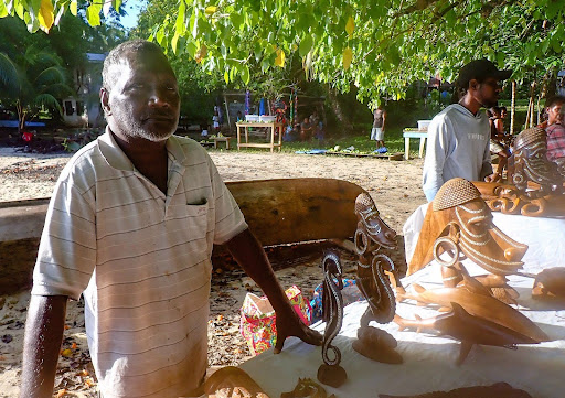 Solomon Islander standing by table of wood carvings