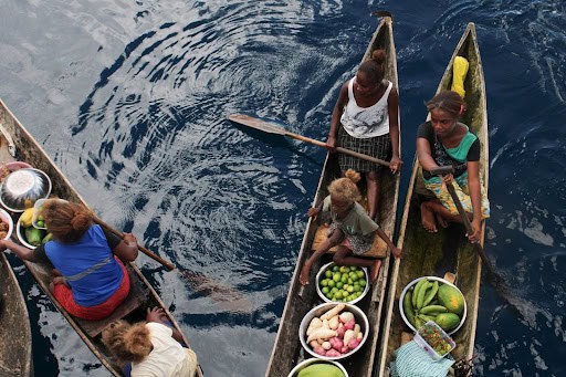 a group of Solomon Islanders on dugout canoes with produce
