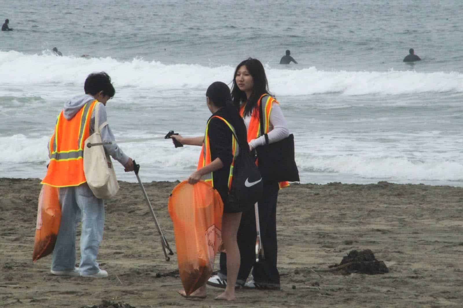 Three volunteers with Oceanic Society picking up trash on a San Francisco beach.