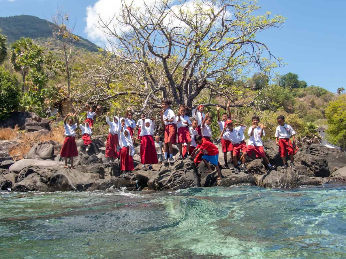 Alorian school children stand at edge of water waving to snorkelers