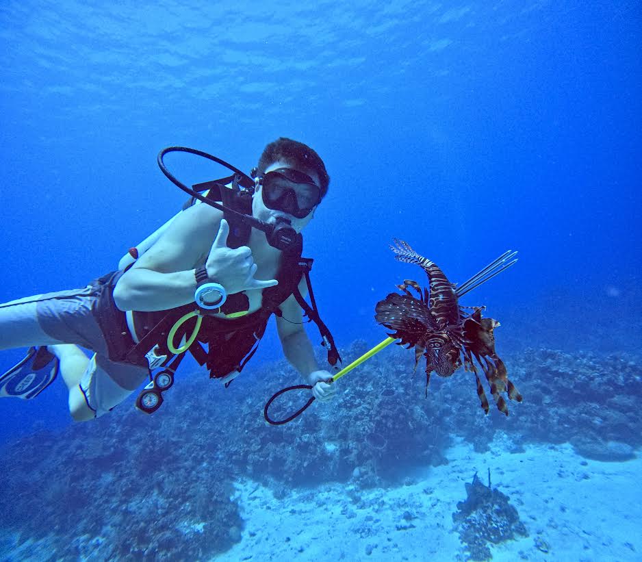 Scuba diver giving a shaka sign while holding a pole spear with a speared lionfish, on a reef in the Caribbean
